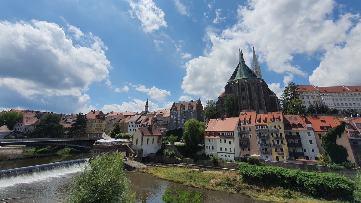 Blick über einen Fluss auf eine Kirche und mehrere Häuser einer Altstadt